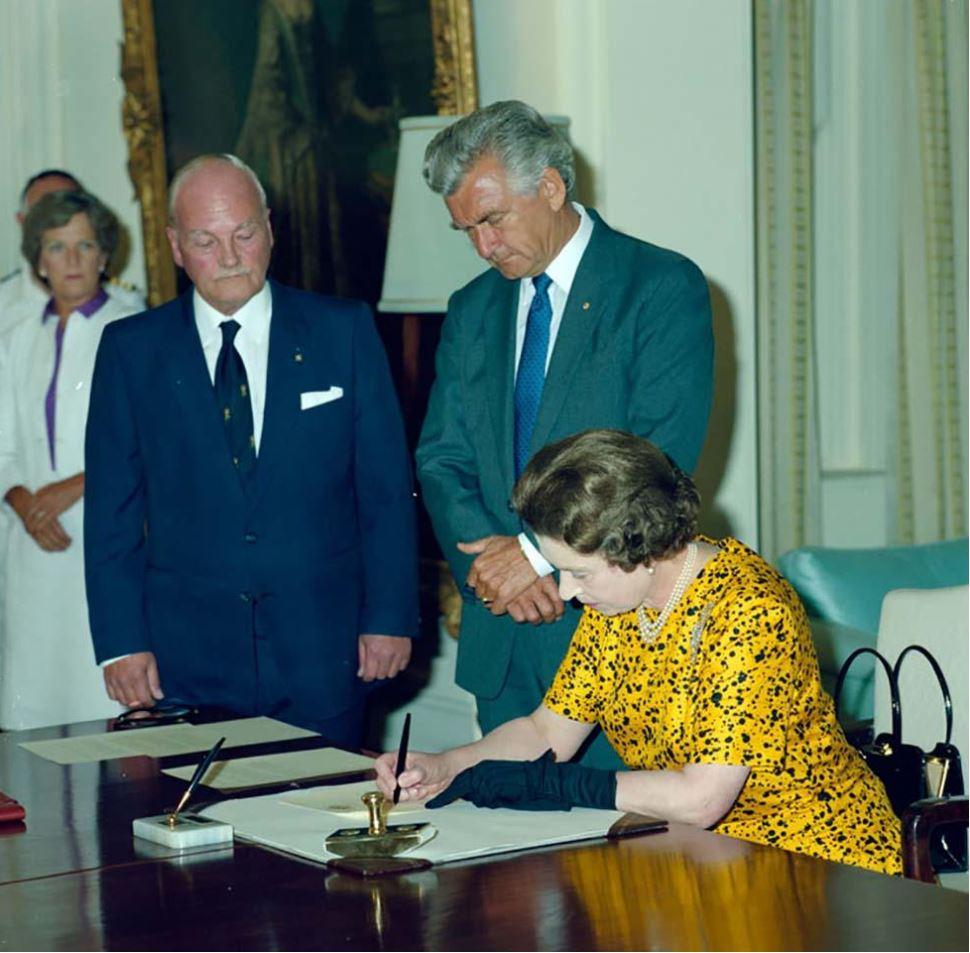 Queen Elizabeth II at Government House, Canberra, signing the Proclamation for the Australia Act (Cth) on 2 March 1986, with Prime Minister RJ ‘Bob’ Hawke looking on.