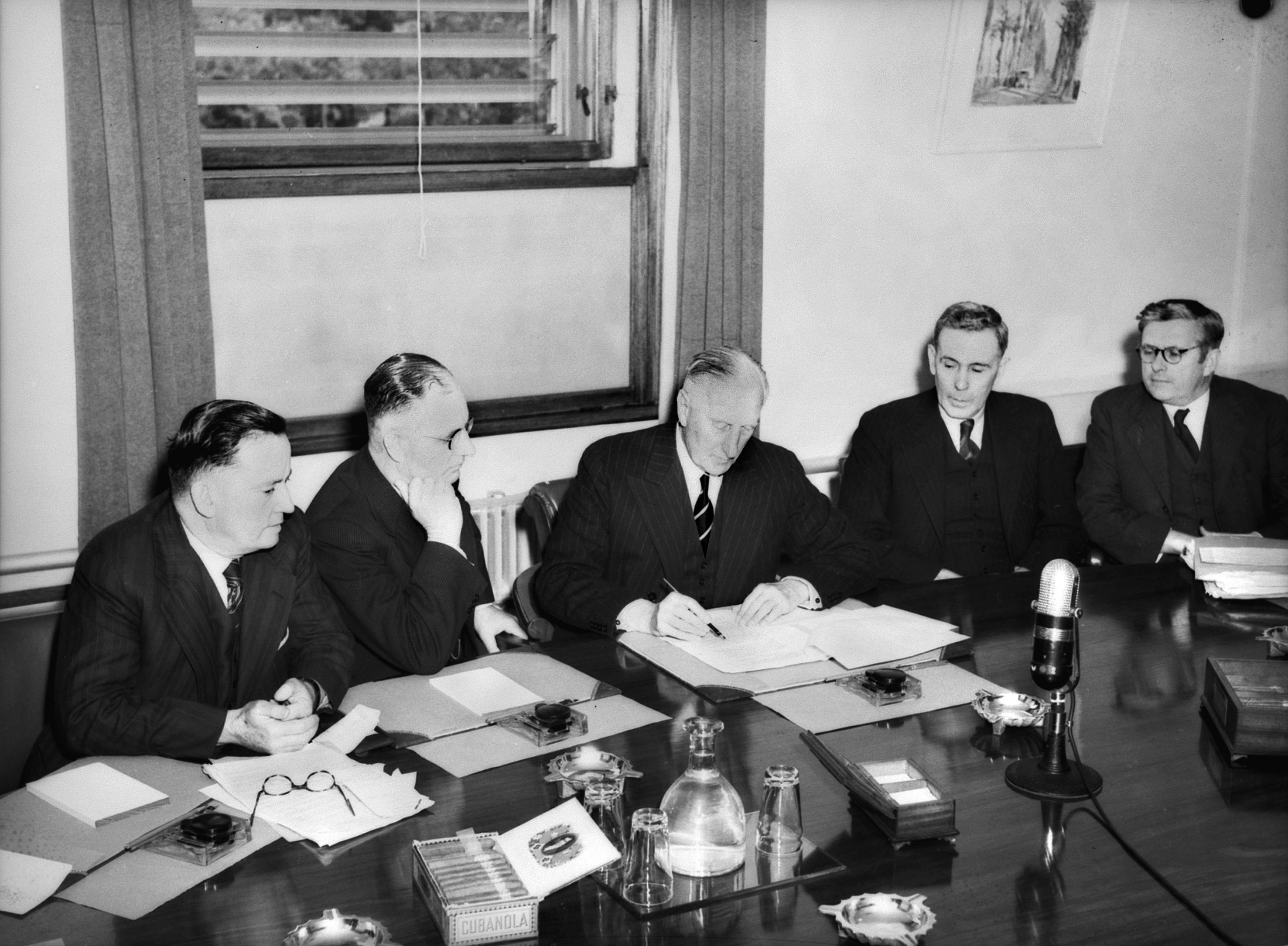 Governor General Lord Gowrie (C) signs the Proclamation of a state of war with Japan, watched by Prime Minister John Curtin (on his right) and other members&nbsp;of the Cabinet, December 1941.
